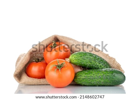 Three ripe tomatoes and two cucumbers with a jute bag, macro, isolated on a white background.