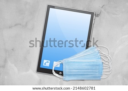 A digital tablet with protective medical mask and on a gray concrete background. 2022 new year concept