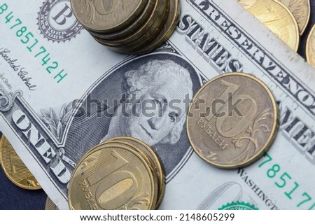 The American dollar on top of which lie Russian coins with a face value of 10 rubles. Translation of the inscriptions on the coins: "10 rubles". close-up
