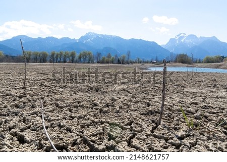 environmental protection, drought in germany and europe, a dried up lake in the alps, in the background mountains and houses Royalty-Free Stock Photo #2148621757
