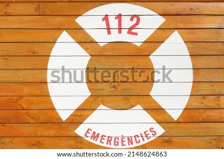 Emergency post in the Castellon tourist resort of El Grau. Signs orange lifebuoy in the foreground and 112 on wooden board. High quality photo