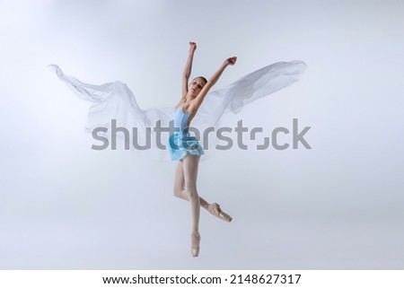 Flying. One young girl, aspiring ballerina in blue dress and pointes dancing with cloth isolated on gray background. Art, beauty, ballet school concept. Copy space for ad