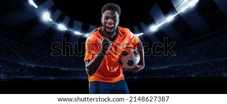 Winner emotions.Excited professional soccer, football player in football kit standing with ball and shouting over dark night stadium with flashlights background. Sport, competition, championship, wow Royalty-Free Stock Photo #2148627387