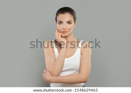 Young beautiful woman with hand on chin smiling wearing white shirt over white background 