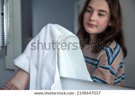 A young woman wipes a mirror in the bathroom with a rag.