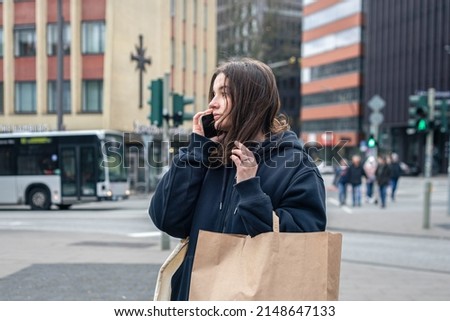 A young woman in the city talking on the phone with a package in her hands, the concept of shopping, city walk.