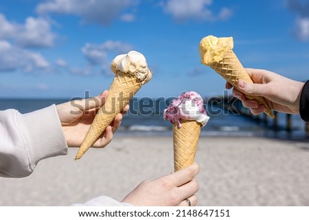 Three waffle cones with appetizing ice cream in female hands against the backdrop of the sea.