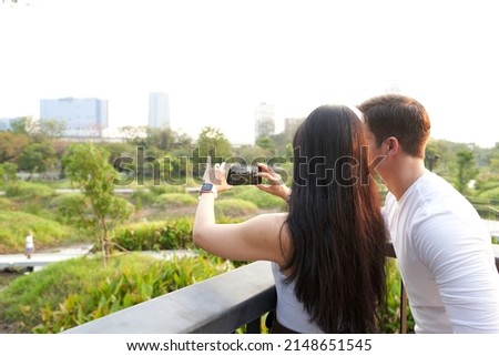 Couple taking photos of the cityscape with the mobile from a park at sunset