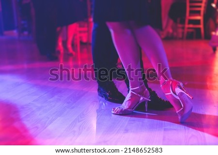 Dancing shoes of a couple, couples dancing traditional latin argentinian dance milonga in the ballroom, tango salsa bachata kizomba lesson, festival on a wooden floor, purple, red and violet lights
