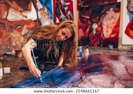 Portrait of a gorgeous redhead female artist working on several art projects on her bright studio. Young Caucasian artistic woman using painting tools on a canvas while drawing picture in studio