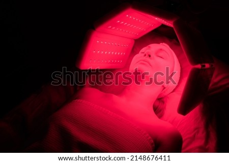 An elderly woman undergoes a facial rejuvenation procedure. Woman face lt Red light treatment At beauty clinic. Cosmetology.