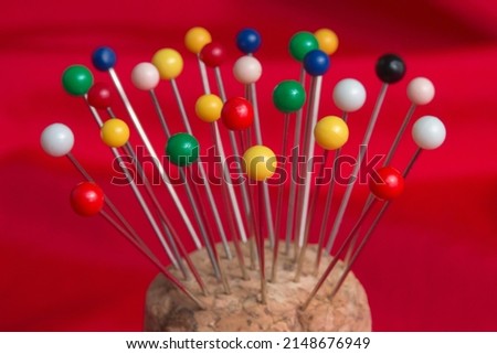 Closeup view of colorful ball head straight pins for sewing in a cork pincushion with a bright red fabric background. Shallow depth of field.