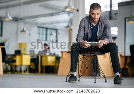 Hes a tech savvy young designer. Shot of a young man using a digital tablet while sitting in a modern office. Royalty-Free Stock Photo #2148702623