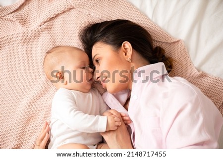 A portrait of a beautiful young mother and her sweet baby in light clothes in their bedroom at home. Lifesthal. Motherhood. Happy family. High quality photo