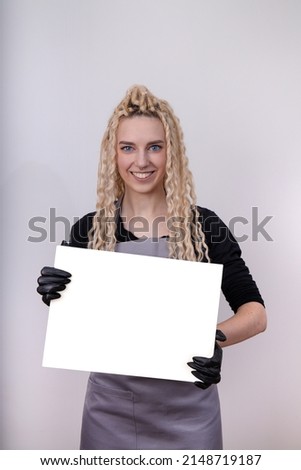 Happy european blonde girl with long hair holding a blank horizontal canvas in her hands, poster mockup with blank frame. A specialist in the field of manicure, hairstyles, tattoo holds a certificate.