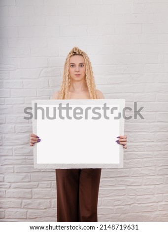 European blond girl with long hair holds blank horizontal canvas in her hands, poster mockup with blank frame. A specialist in the field of manicure, hairstyles, tattoo holds a certificate.