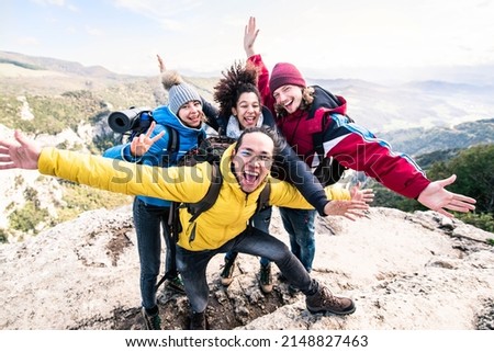 Group of hikers climbing mountains - Happy friends with hands up on the top of the mountain - Multiethnic people having trekking day out together 