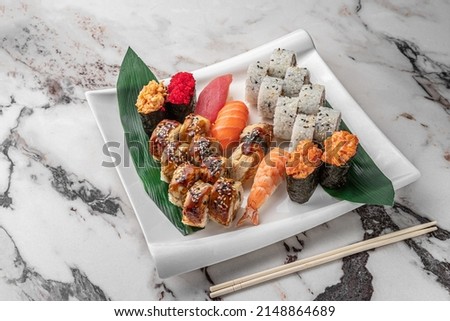 set of different colorful maki sushi rolls, nigiri and gunkan with tiger shrimp, tomago, salmon, tuna, chuka salad, flying fish caviar, tuna and green bamboo leaf in a white ceramic plate, side view