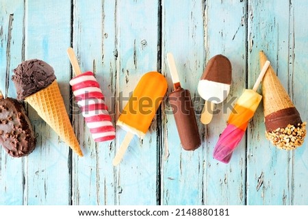 Variety of chocolate and colorful summer popsicles and ice cream treats. Top view scattered on a rustic blue background. Royalty-Free Stock Photo #2148880181