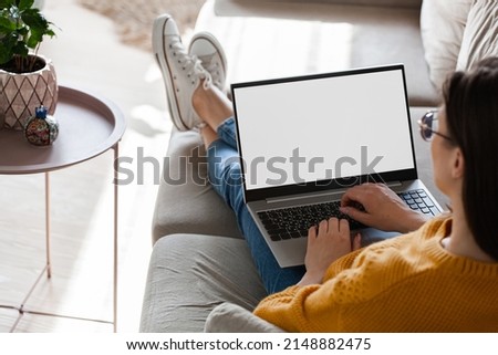 Young woman using laptop screen blank, mockup lying on sofa at home