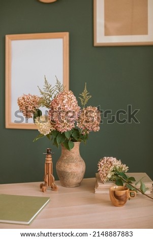 Still life with hydrangea flowers in vase, stylish ceramic cup, candle holder, wooden picture frame mock up on the wall.