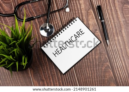 Healthcare text on note pad with stethoscope, pen and green potted plant - Health and medicine concept