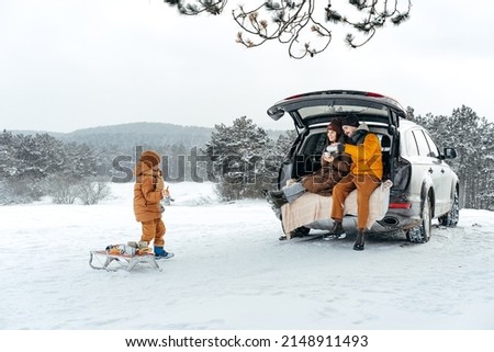 Winter portrait of a family sit on car trunk enjoy their vacation in forest