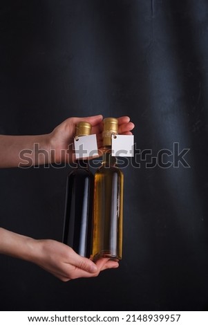 Female hands holding two 250 ml bottles of red and white wine with blank label, no brand mock up on black background. Vertical shot, copy space