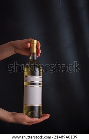 Hands holding bottle of white wine with template label, no brand. Riesling, chardonnay, sauvignon blanc. Alcohol beverage on black background
