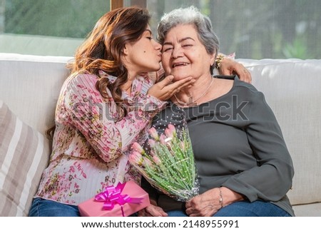 Happy Mother's Day! Hispanic mom and daughter kiss, hug and give each other flowers and gifts on a special day. Royalty-Free Stock Photo #2148955991