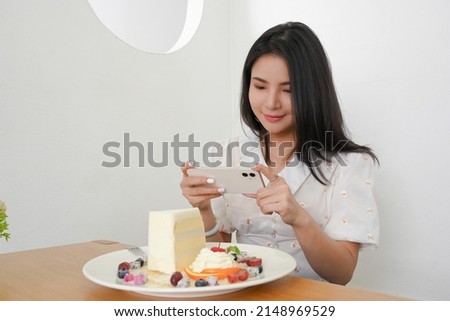 Beautiful Asian millennial woman taking a yummy desserts photo with her smartphone in the cafe.