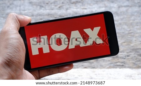 Hand holding smartphone with letter HOAX on red background. Propaganda, disinformation and hoax concept. Royalty-Free Stock Photo #2148973687