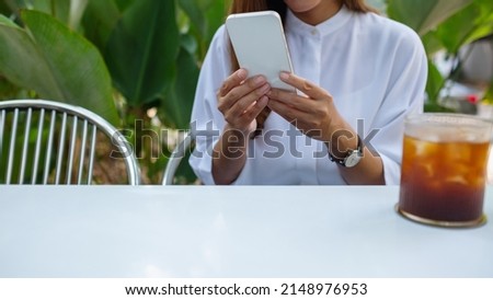 Closeup image of a young woman holding and using mobile phone with coffee cup on the table