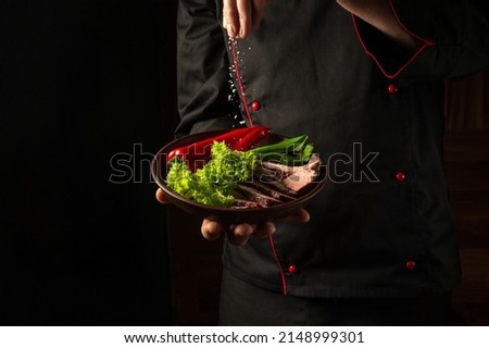 Grilled and sliced beef steak with grilled vegetables served on plate on black background presentation in chef hands