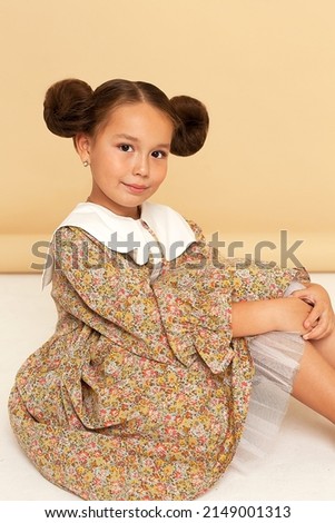 Photo of a cute little beautiful girl in the studio on a brown background. The girl is dressed in a lush yellow dress, looks at the camera and smiles. Art photography. Autumn photo shoot..