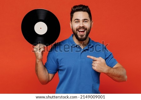 Young excited happy satisfied amazed cool DJ man 20s in basic blue t-shirt hold point finger on retro vintage music plate isolated on plain orange background studio portrait. People lifestyle concept