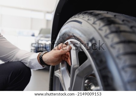 Close cropped up photo shot man hand buyer client in shirt chooses auto wants to buy new automobile touch car tire wheel disk in showroom vehicle salon dealership store motor show indoor Sales concept