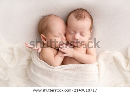 Tiny newborn twins boys in white cocoons on a white background. A newborn twin sleeps next to his brother. Newborn two twins boys hugging each other.Professional studio photography Royalty-Free Stock Photo #2149018717