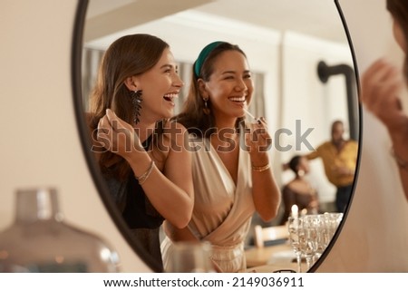 We always have a joke prepared. Shot of two young friends standing together and using a mirror to touch up their makeup at a dinner party. Royalty-Free Stock Photo #2149036911