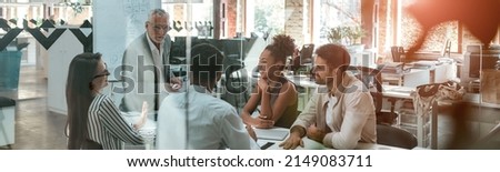 Business meeting. Mature businessman discussing something with his young colleagues while sitting together at the office table in the modern office