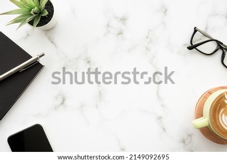 White marble desk table with cup of latte coffee and notebook with pen. Top view with copy space, flat lay.