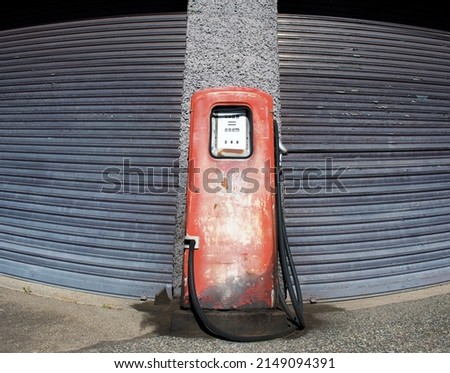 No more petrol. Old, red, rusty petrol pump in front of neutral roller garage door. Out of service, oil embargo.