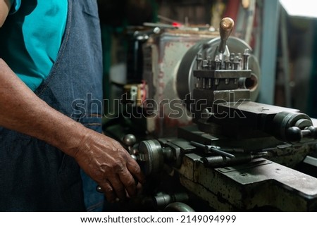 Close Up A senior Asian man preparing steel turning equipment. He is a small industrial steel turner who specializes and is professional in turning steel. Royalty-Free Stock Photo #2149094999