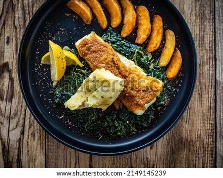 Fish dish - roast cod fillet with potatoes and spinach served on stone plate on wooden table