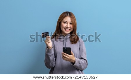 Portrait of beautiful Asian woman holding credit card and mobile phone on isolated background, portrait concept used for advertisement and signage, isolated over blue background, copy space.