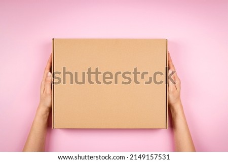 Female hands holding brown cardboard box on pastel pink background. Top view to mockup parcel box. Packaging, shopping, delivery concept Royalty-Free Stock Photo #2149157531