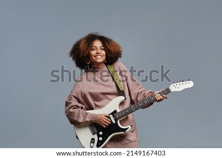 Minimal waist up portrat of curly haired black girl playing electric guitar and smiling at camera, copy space Royalty-Free Stock Photo #2149167403