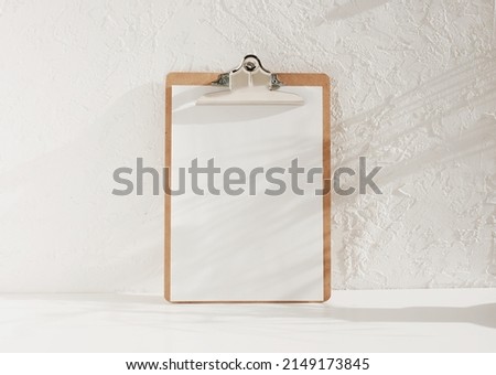 wooden clipboard with blank a4 paper with copy space on white background with floral shadows. Minimal concept.menu board, business template. Royalty-Free Stock Photo #2149173845