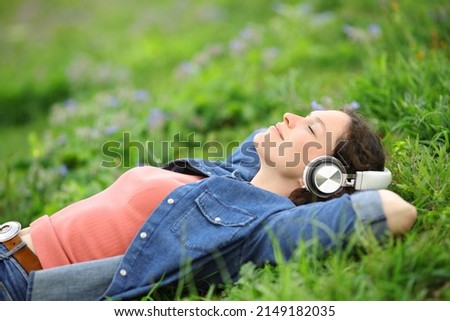Relaxed woman lying on the grass listening to music with headphones in a park Royalty-Free Stock Photo #2149182035