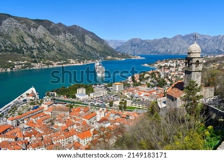 Kotor, Montenegro, Europe. Bay of Kotor on Adriatic Sea. Church, roofs of the historical buildings in the old town. Bay and mountains in the background. Clear blue sky, sunny day.